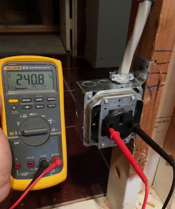 Digital multimeter reading 240.8 volts near electrical outlet installation.