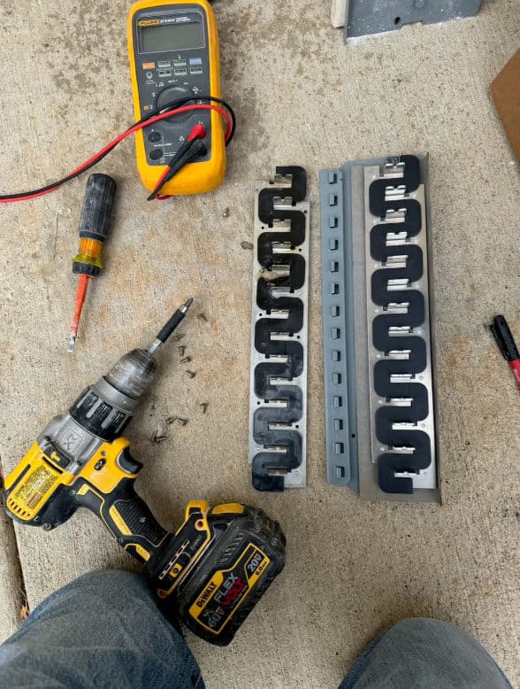 Tools and hardware on concrete: a drill, multimeter, screws, and metal strips.