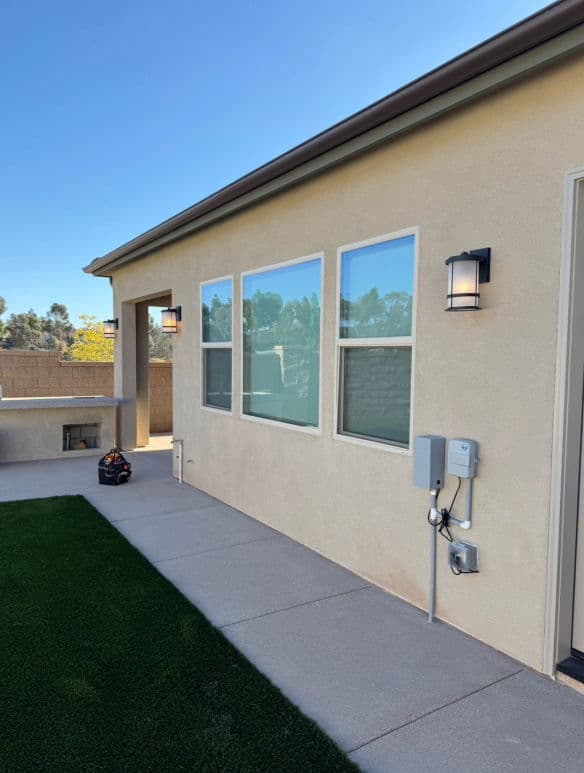 Exterior view of a modern home with large windows and patio, featuring landscaping and utility box.