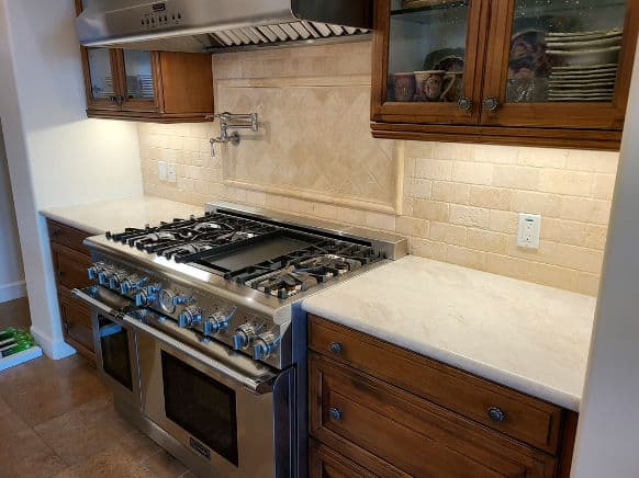 Modern kitchen with a large gas stove, wood cabinets, and elegant tile backsplash.