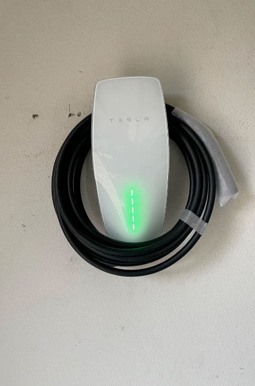 Tesla electric vehicle charger mounted on wall with charging indicator light illuminated.