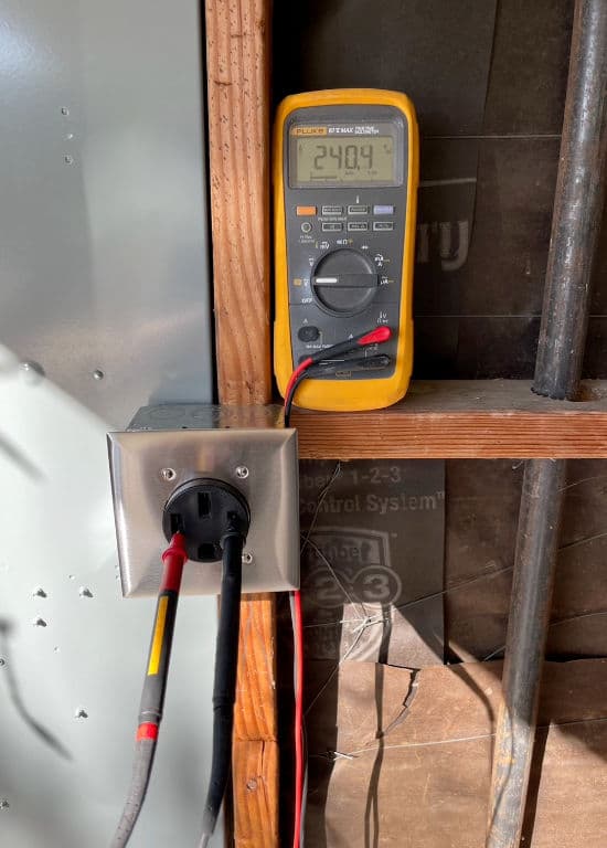 Digital multimeter displaying 240.9 volts connected to electrical outlet in a wall.