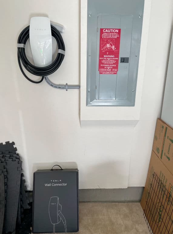 Tesla Wall Connector mounted on the wall next to an electrical panel with safety warning.