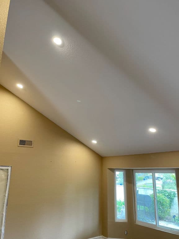 Modern room with recessed lighting and a high ceiling, featuring a large window and beige walls.