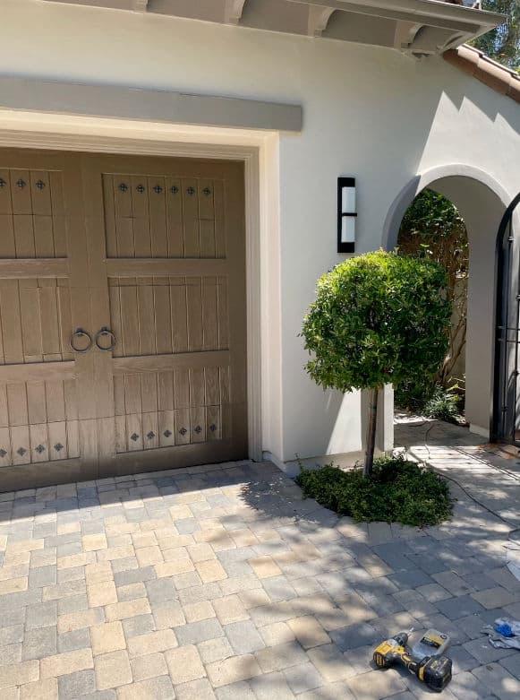 Charming home exterior featuring a garage door, landscaped tree, and stone pavers.