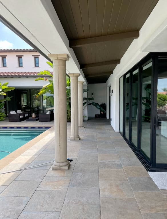 Luxury home patio with columns, pool, and tropical plants in a sunny outdoor setting.